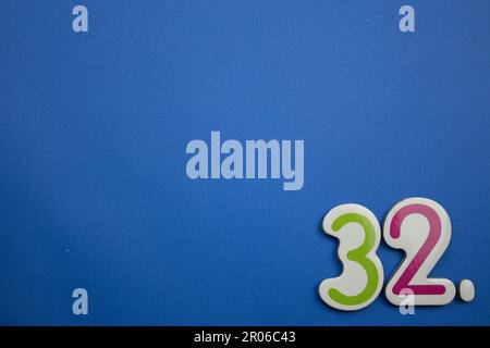 The number 32, placed on the edge of a blue background, photographed from above, colored green and red. Stock Photo