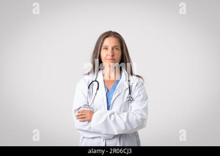 The face of modern healthcare. Portrait of confident senior doctor woman posing with folded arms, light background Stock Photo