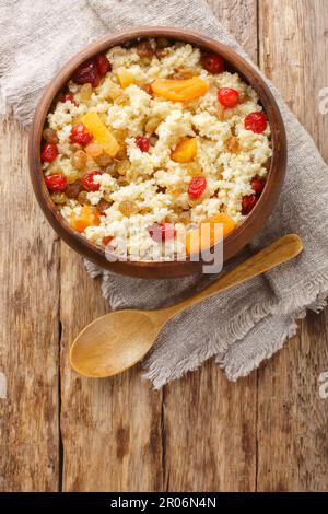 Sweet millet porridge with raisins and dried apricots, cherries close-up in a bowl on the table. Vertical top view from above Stock Photo