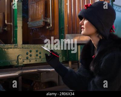 Attractive young woman in red 1920s flapper dress and cloche hat travelling by antique steam train Stock Photo