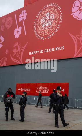 Police stand guard beneath London's iconic National Gallery in Trafalgar Square which is adorned with a massive red hoarding in honour of the coronati Stock Photo