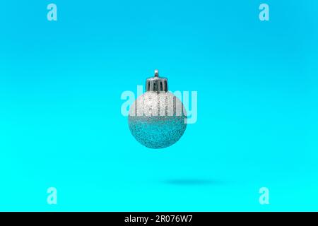 Silver Christmas Ball Ornament Floating in Mid-Air on a Blue Background Stock Photo