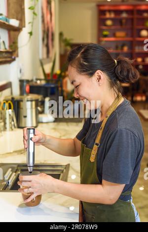 Vietnamese barista using a mixer for condensed milk in glass cup for preparing vietnamese coffee Cafe Sua Stock Photo