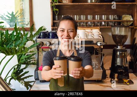 Vietnamese smiling waitress holding paper cups with coffee in a cafe Stock Photo