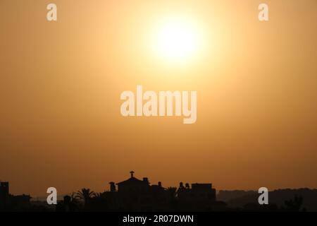 The sun is setting over a building in the distance Stock Photo