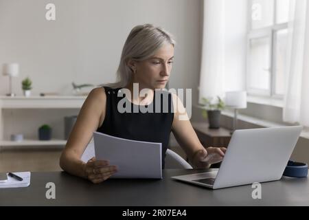 Serious senior freelance business woman checking paper invoice Stock Photo