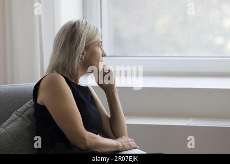 Thoughtful depressed mature woman sitting on couch at home Stock Photo
