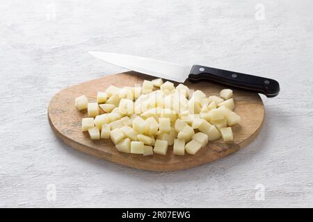 Wooden board with fresh diced potatoes on a light gray background. Stage of cooking vegetable stew Stock Photo