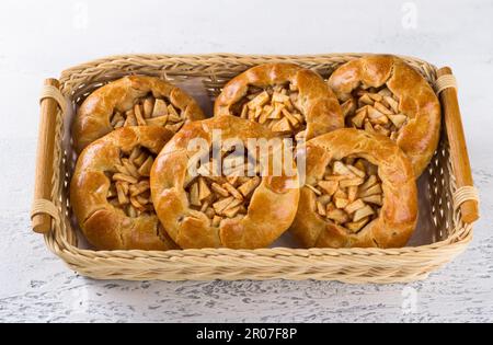 Sweet mini pies with apples and cinnamon in a wicker basket on a light gray background. Delicious homemade food Stock Photo