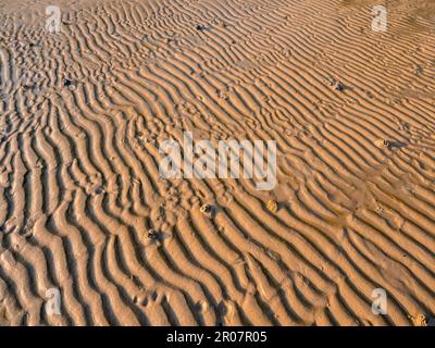 Sandy pattern and texture on the beach created by waves and sea breezes on sunset. Wet sand beach background for summer holiday and tropical travel va Stock Photo