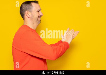 Bearded hispanic man in profile wearing a red jumper feeling happy, smiling and clapping with grateful emphasis for the great show he just witnessed Stock Photo