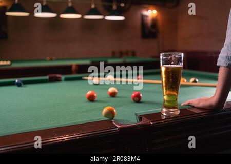 Male hand, colorful billiard balls and pool stick on pool table with glass of beer Stock Photo