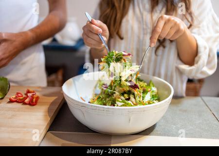 Female hands mixing green salad in the bowl with forks Stock Photo