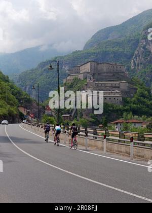 Cyclists pass by Fort of Bard (Forte di Bard) in the Aosta Valley, NW Italy Stock Photo