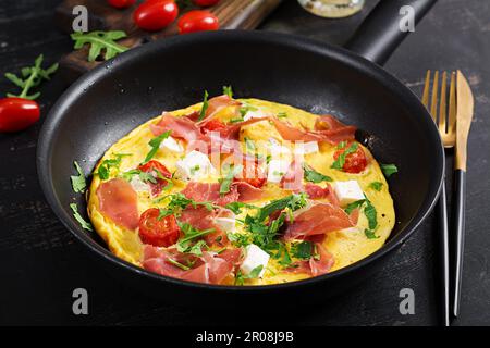Omelet with tomatoes, jamon and feta cheese in pan. Stock Photo