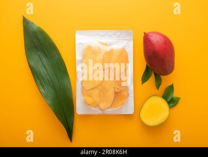 Large pack of dried mango slices with leaf and raw mango on yellow background.Top view. Stock Photo