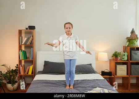 Joyful girl jumping on bed, having fun at home after school Stock Photo