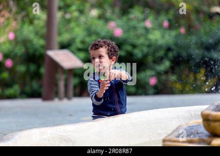 child playing with a leaf next to a fountain Stock Photo