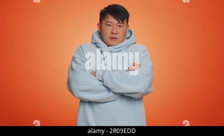 Offended sad nervous asian man having misunderstanding, frustrated after quarrel, fail, lose, ignores and does not want to communicate, talk. Guy isolated on orange studio background. People lifestyle Stock Photo