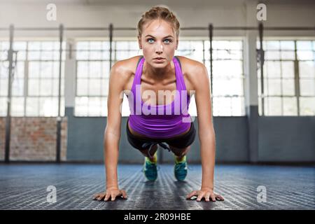 Your workout is my warmup. a sporty young woman doing push-ups at the gym. Stock Photo