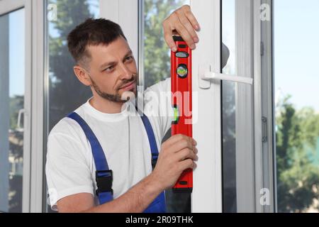 Worker using bubble level after plastic window installation indoors Stock Photo