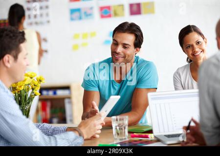 Sharing his creative ideas. A handsome young man sitting at a table in a working a environment and sharing ideas with his colleagues. Stock Photo