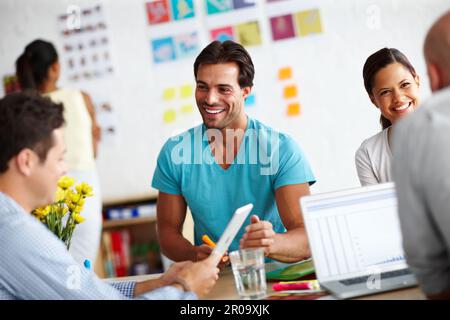 Hes a people person. A handsome young man sitting at a table in a working a environment and sharing ideas with his colleagues. Stock Photo