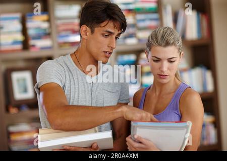 Focussed on their studies. two college students with textbooks discussing work in the library. Stock Photo