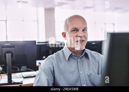aged man caught in the act of saying something while working with his workstation in a room full of computers. He stares at you entrusting you with so Stock Photo