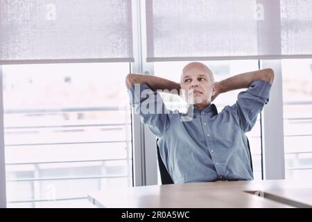 Man in office relaxes with arms crossed behind his head, dreaming of vacation, weekend or retirement Stock Photo