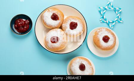 Hanukkah sweet doughnuts sufganiyot (traditional donuts) with fruit jelly jam and white candles on blue paper background. Jewish holiday Hanukkah conc Stock Photo