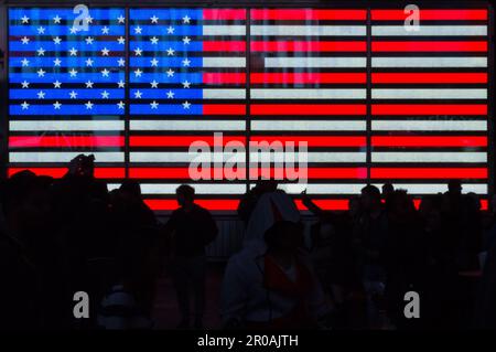 A crowd gathers in front of an illuminated flag in New York City’s Times Square. Stock Photo