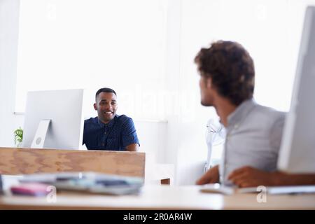 Dude, what are you working on at the moment. A handsome young businessman sitting at his desk with his colleague in the background. Stock Photo
