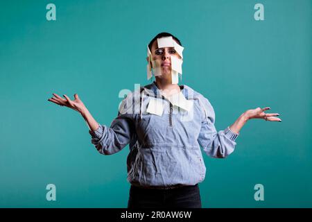 Tired overworked woman writes down memo messages using paper sticky notes, helping her with plenty details about work. Colorful memory reminder on busy exhausted employee, studio shot Stock Photo
