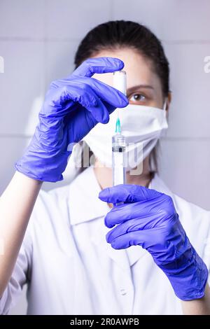 A young woman doctor draws medicine from an ampoule into a syringe.  Close-up.  Vaccination and immunization.Wearing Blue Latex Gloves And Protective Stock Photo