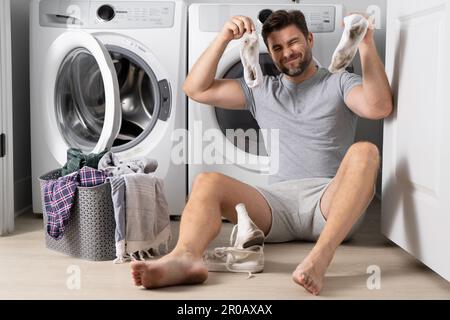 Man with clothes near washing machine. Laundry cleaning. Housework, homework, male housekeeper. Husband man doing laundry at home. Washer and dryer at Stock Photo