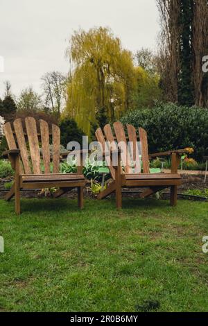 Two Wooden lounges chairs placed on spacious terrace of modern country house surrounded with green plants garden furniture outdoor for relaxing on summer days. Garden landscape with two chairs in nature. Backyard exterior  Stock Photo
