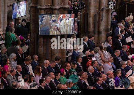 Guests and members of the congregation watch the Coronation rituals on screens inside the Westminster Abbey of The King Charles III and Queen Consort. Stock Photo