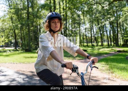 Young woman in helmet riding on bicycle at park Stock Photo