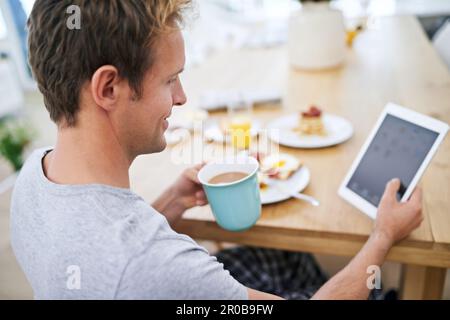 Having a relaxed breakfast. a handsome man using his tablet while having breakfast at home. Stock Photo