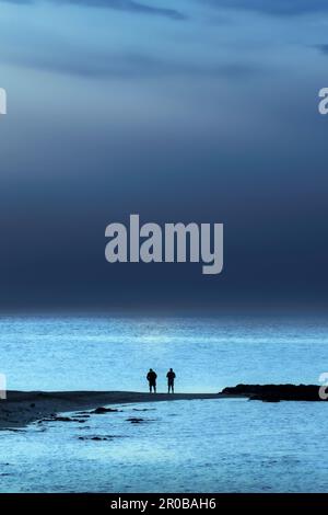 Two men looking out over the sea from beach towards an approaching storm. Stock Photo