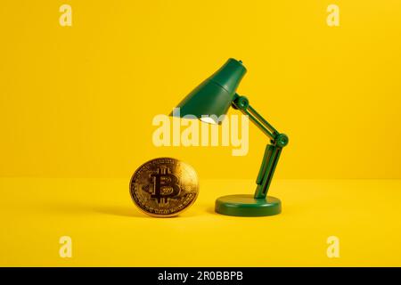 Golden bitcoin iluminated by a green toy lamp on yellow background Stock Photo