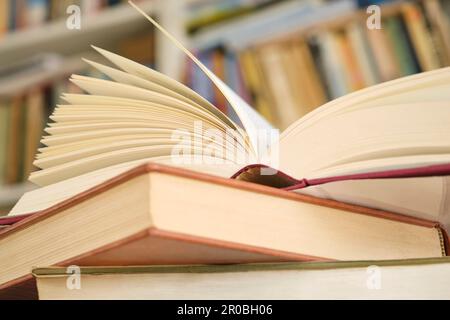 Open book or textbook on a pile of closed books in front of a bookcase in a library. Education learning concept. Image with selective focus. Stock Photo