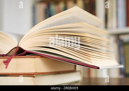 Open book or textbook on a pile of closed books in front of a bookcase in a library. Education learning concept. Image with selective focus. Stock Photo