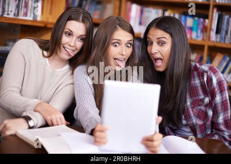 Too much studying can do strange things. three friends sitting in the library taking photos of themselves with a digital tablet. Stock Photo