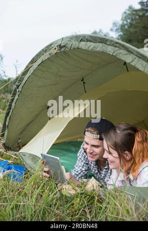 Young couple using digital tablet in camp tent, Bavaria, Germany Stock Photo