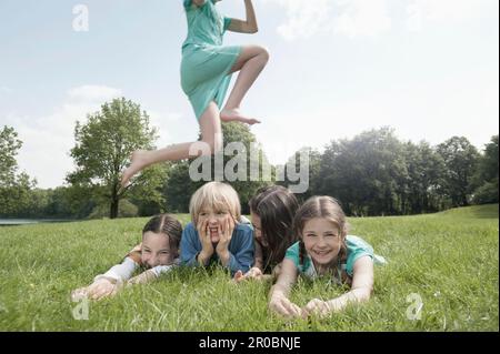 Girl jumping over her friends lying on grass in a park, Munich, Bavaria, Germany Stock Photo