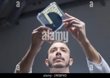 Young male scientist looking at laboratory equipment in an optical laboratory, Freiburg im Breisgau, Baden-WÃ¼rttemberg, Germany Stock Photo