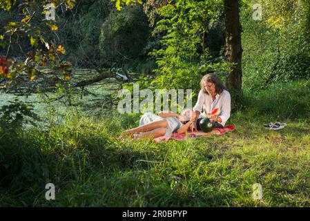Couple having picnic and eating watermelon at riverbank, Bavaria, Germany Stock Photo
