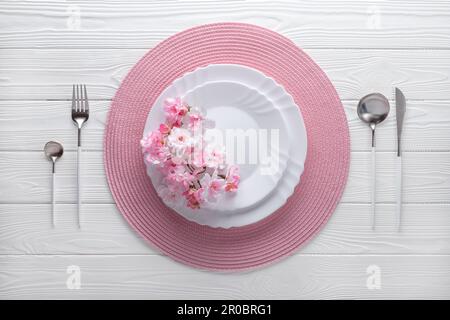 Festive place setting with pink napkin and spring flowers. Empty plates and silver cutlery on white wooden table. Top view. Festive dinner in luxury r Stock Photo